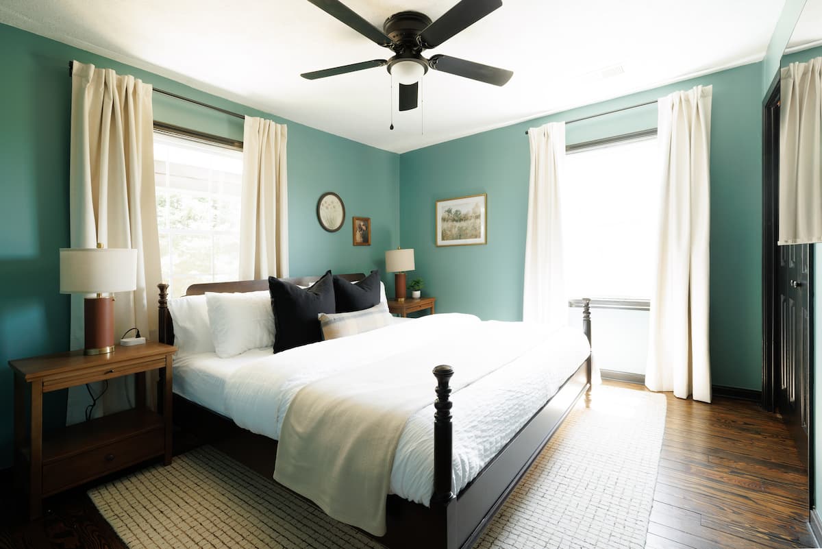 King bedroom with blue-green walls, dark metal bed, and bright windows