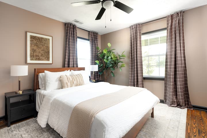 Queen bedroom with soft neutral walls, white bedding, and plaid curtains